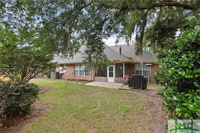 rear view of property featuring a lawn, brick siding, a patio, a shingled roof, and central air condition unit