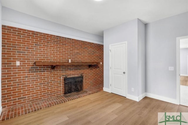 unfurnished living room with baseboards, wood finished floors, and a brick fireplace