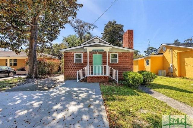 bungalow-style home with brick siding, a front yard, central AC unit, and a chimney