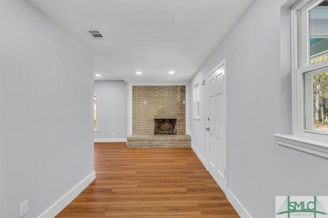 unfurnished living room with a brick fireplace, light wood-type flooring, baseboards, visible vents, and recessed lighting