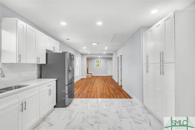 kitchen featuring light countertops, stainless steel refrigerator with ice dispenser, marble finish floor, a sink, and white cabinets