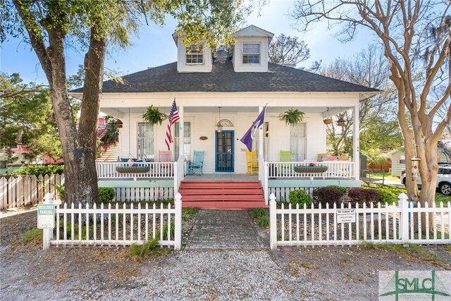 bungalow-style home featuring covered porch, a fenced front yard, and roof with shingles