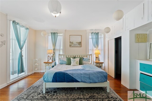 bedroom with multiple windows, wood finished floors, and baseboards