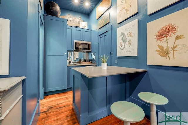 909 Howard St, Savannah, GA 31401 - kitchen featuring light countertops, light wood finished floors, a kitchen bar, stainless steel microwave, and blue cabinetry