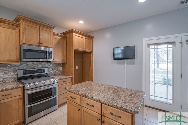 402 Walthour Dr, Rincon, GA 31326 - kitchen featuring appliances with stainless steel finishes, light tile patterned flooring, decorative backsplash, light stone countertops, and a kitchen island