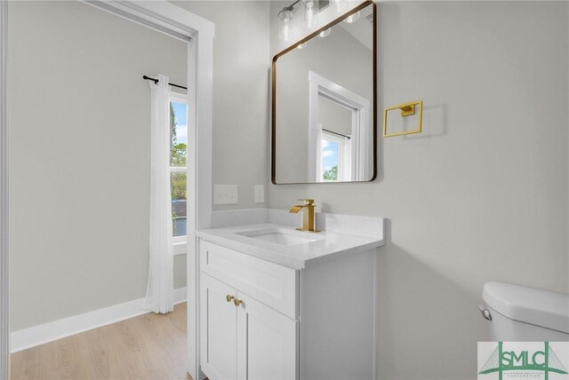 half bath featuring toilet, a wealth of natural light, vanity, and wood finished floors