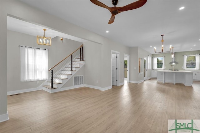 unfurnished living room featuring recessed lighting, baseboards, ceiling fan with notable chandelier, light wood-style floors, and stairway