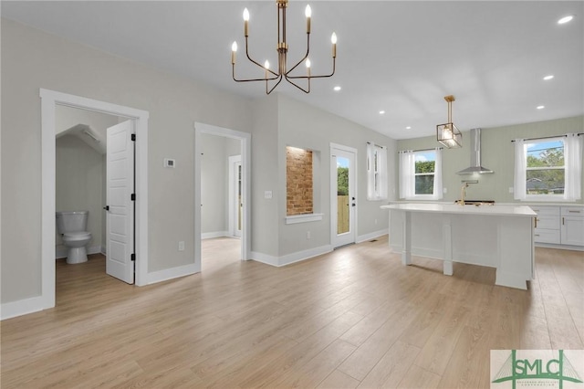kitchen featuring wall chimney exhaust hood, a center island with sink, recessed lighting, light countertops, and light wood-style floors