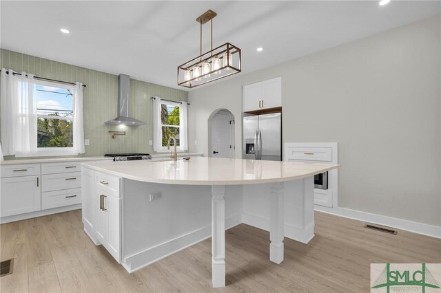 kitchen with visible vents, wall chimney exhaust hood, white cabinetry, stainless steel fridge, and light countertops