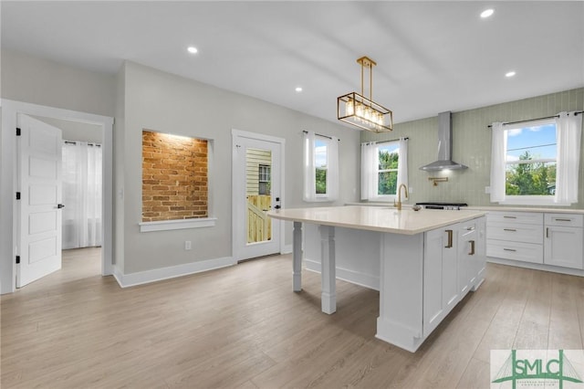 kitchen with light wood finished floors, a healthy amount of sunlight, light countertops, and wall chimney exhaust hood