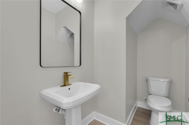 bathroom with toilet, baseboards, visible vents, vaulted ceiling, and wood finished floors