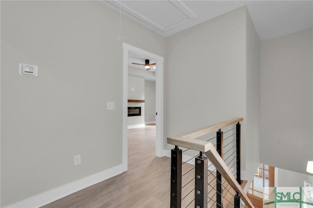 hall with baseboards, light wood-style floors, and an upstairs landing