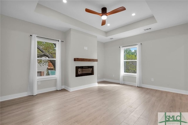unfurnished living room with a tray ceiling, plenty of natural light, visible vents, and light wood-type flooring