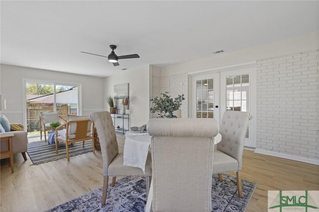 living area featuring light wood-type flooring, french doors, brick wall, visible vents, and a ceiling fan