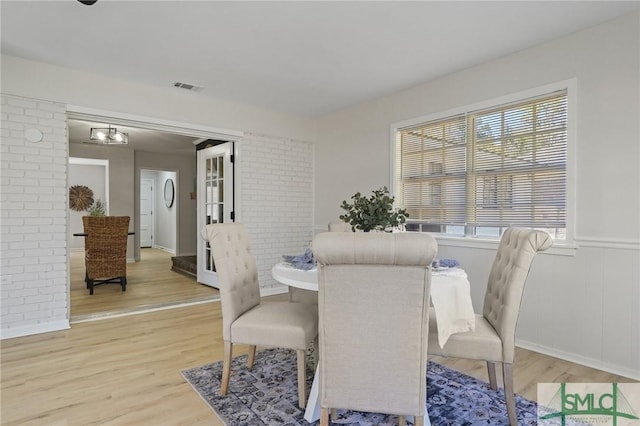 dining room with light wood-style flooring, visible vents, wainscoting, and brick wall