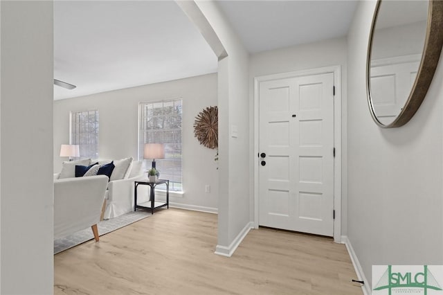 entrance foyer with arched walkways, baseboards, and light wood finished floors