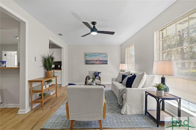 living room featuring baseboards, visible vents, light wood-style flooring, and a ceiling fan