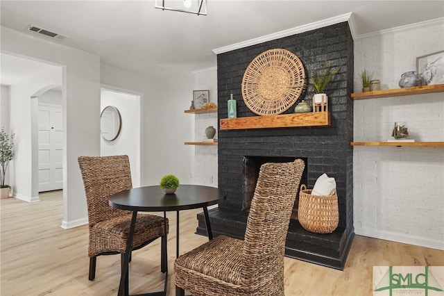 dining area featuring a fireplace, baseboards, visible vents, light wood-style floors, and ornamental molding