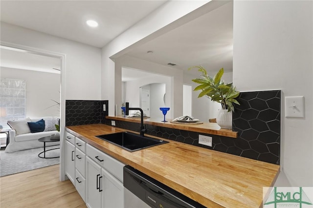 kitchen with a sink, white cabinetry, butcher block countertops, light wood-type flooring, and open floor plan