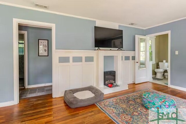 living room featuring baseboards, visible vents, crown molding, and wood finished floors