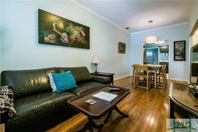 living area with baseboards, visible vents, crown molding, and hardwood / wood-style floors