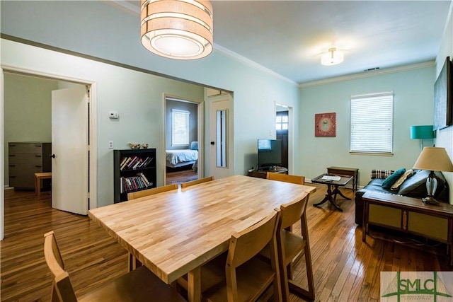 dining room with wood-type flooring, ornamental molding, a healthy amount of sunlight, and visible vents