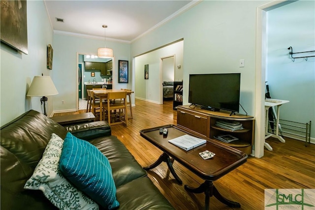 living area featuring wood finished floors, crown molding, baseboards, and visible vents