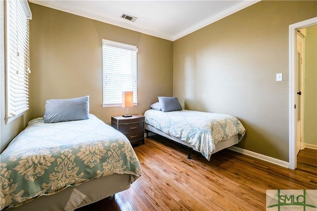 bedroom with baseboards, visible vents, crown molding, and wood finished floors