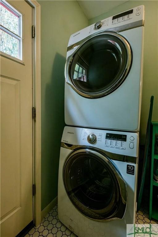 laundry area with baseboards, stacked washer / dryer, laundry area, and light floors
