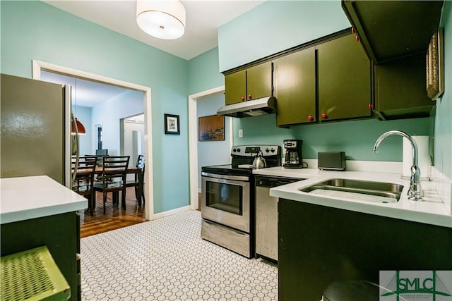 kitchen featuring light countertops, stainless steel appliances, under cabinet range hood, a sink, and green cabinetry