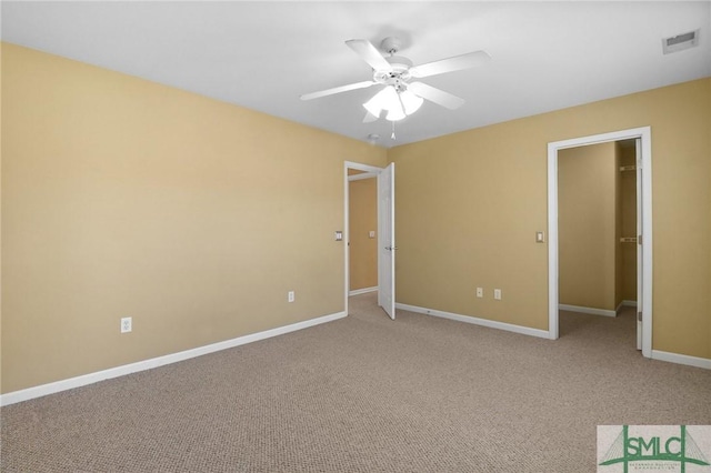 unfurnished bedroom with light colored carpet, a spacious closet, baseboards, visible vents, and a ceiling fan