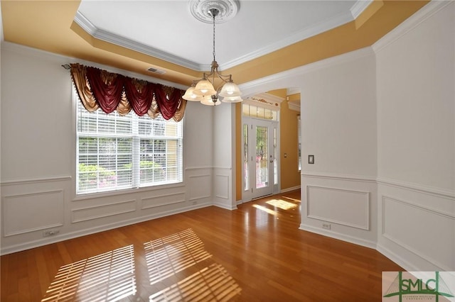 unfurnished dining area with a tray ceiling, an inviting chandelier, visible vents, a decorative wall, and wood finished floors