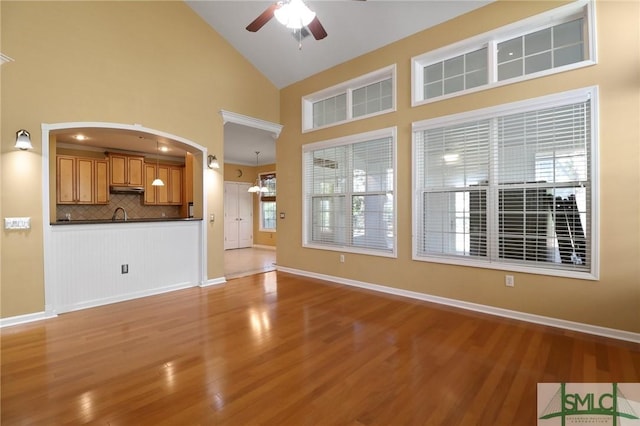 unfurnished living room with wood finished floors, high vaulted ceiling, baseboards, and ceiling fan