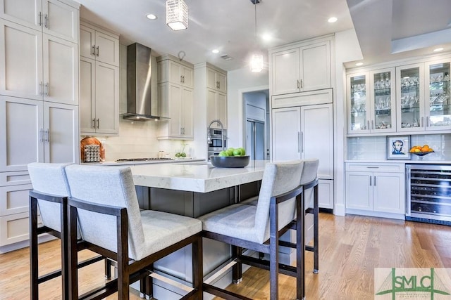 28 Delegal Rd, Savannah, GA 31411 - kitchen featuring wine cooler, wall chimney exhaust hood, a kitchen bar, light wood-type flooring, and decorative light fixtures