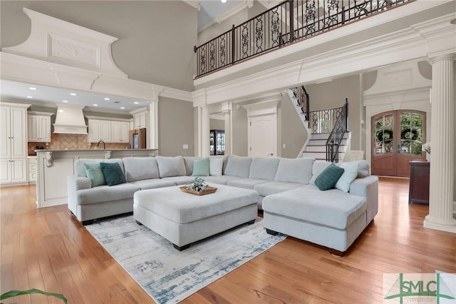 living room with decorative columns, a towering ceiling, stairway, and light wood finished floors