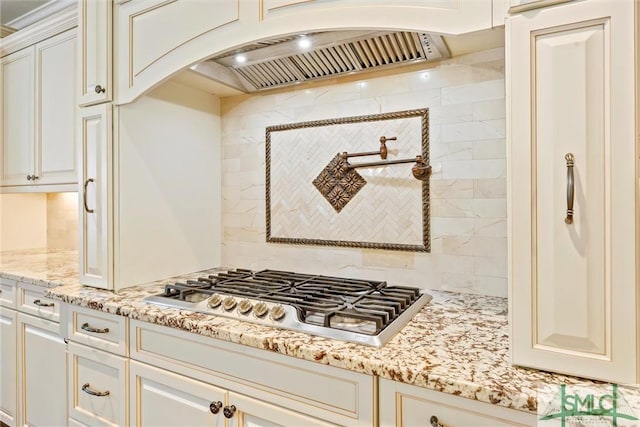 kitchen featuring arched walkways, stainless steel gas cooktop, light stone counters, custom range hood, and backsplash
