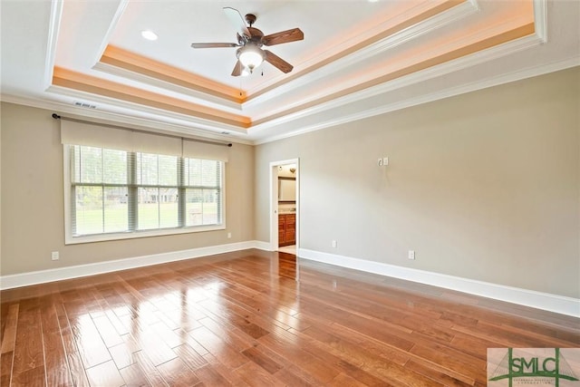 empty room with a tray ceiling, wood finished floors, and baseboards