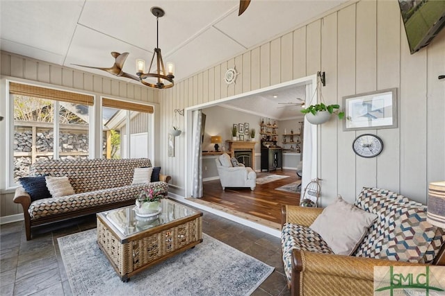 living room with baseboards, ceiling fan with notable chandelier, and stone finish flooring
