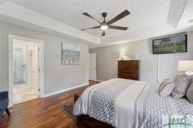 bedroom with a tray ceiling, wood finished floors, a textured ceiling, baseboards, and visible vents