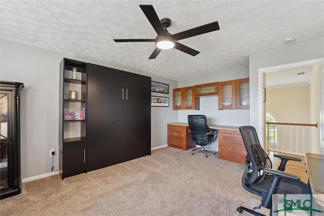 office featuring a textured ceiling, baseboards, light colored carpet, and ceiling fan