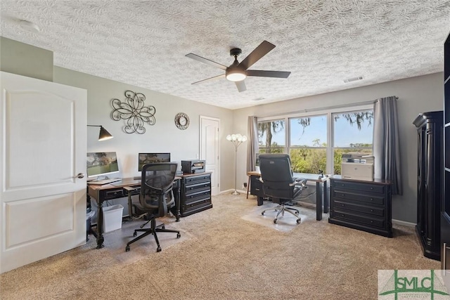 carpeted office space with a textured ceiling, visible vents, ceiling fan, and baseboards