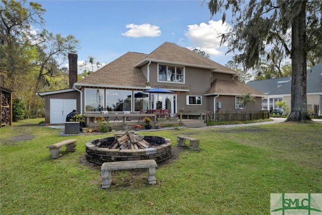 rear view of property with a fire pit, a shingled roof, a yard, and a chimney