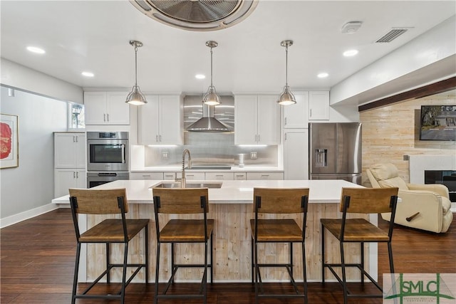 1000 Sea Island Rd Unit 56, Saint Simons Island, GA 31522 - kitchen with appliances with stainless steel finishes, wall chimney range hood, light countertops, a center island with sink, and white cabinetry