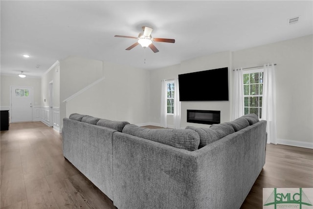 living room with a ceiling fan, wood finished floors, a glass covered fireplace, a decorative wall, and visible vents