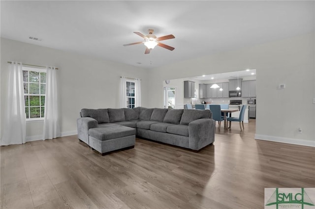 living area with baseboards, visible vents, ceiling fan, and wood finished floors