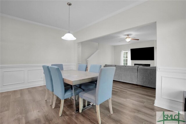 dining space featuring crown molding, a wainscoted wall, ceiling fan, a decorative wall, and wood finished floors