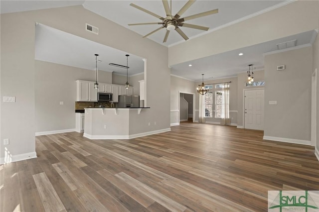unfurnished living room with baseboards, ceiling fan with notable chandelier, ornamental molding, and wood finished floors