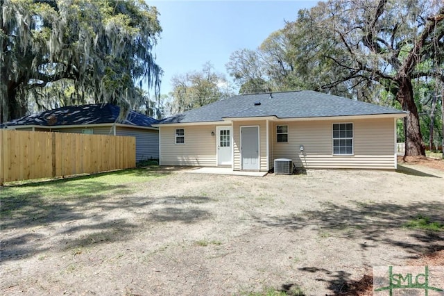 rear view of house with central AC unit, fence, and roof with shingles