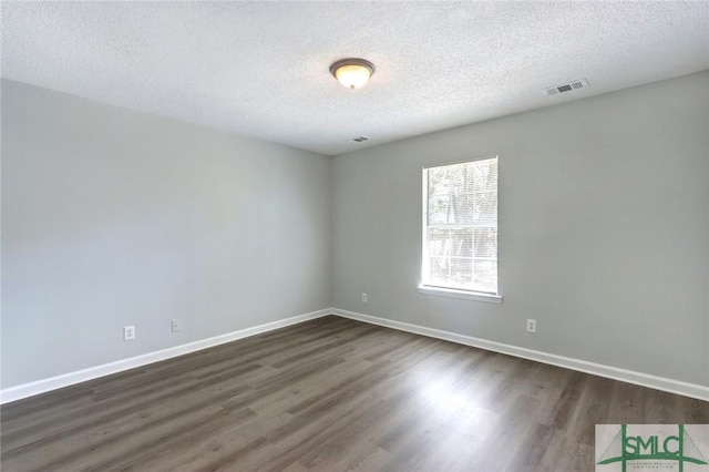empty room featuring dark wood-style flooring, a textured ceiling, baseboards, and visible vents