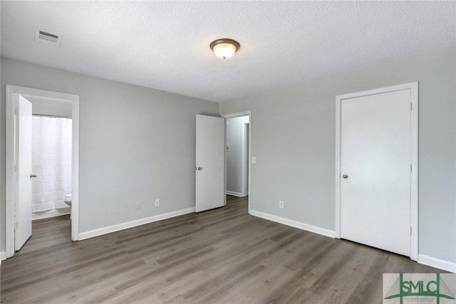 unfurnished bedroom featuring baseboards, visible vents, a textured ceiling, and wood finished floors